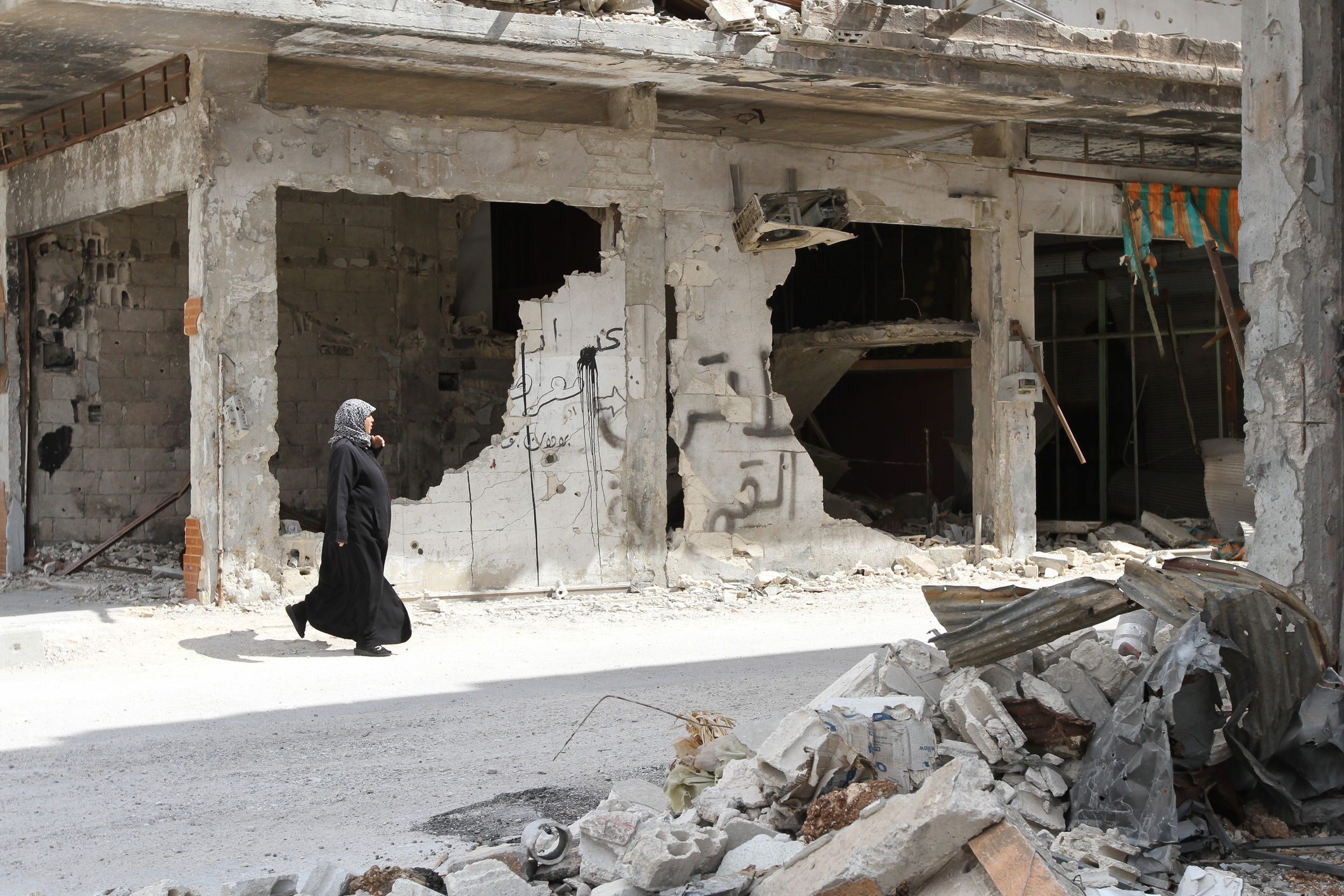 Homs, Syria - September 22, 2013: A woman walks near a house in the city of Homs destroyed in the fighting between the rebels of the Syrian National Army